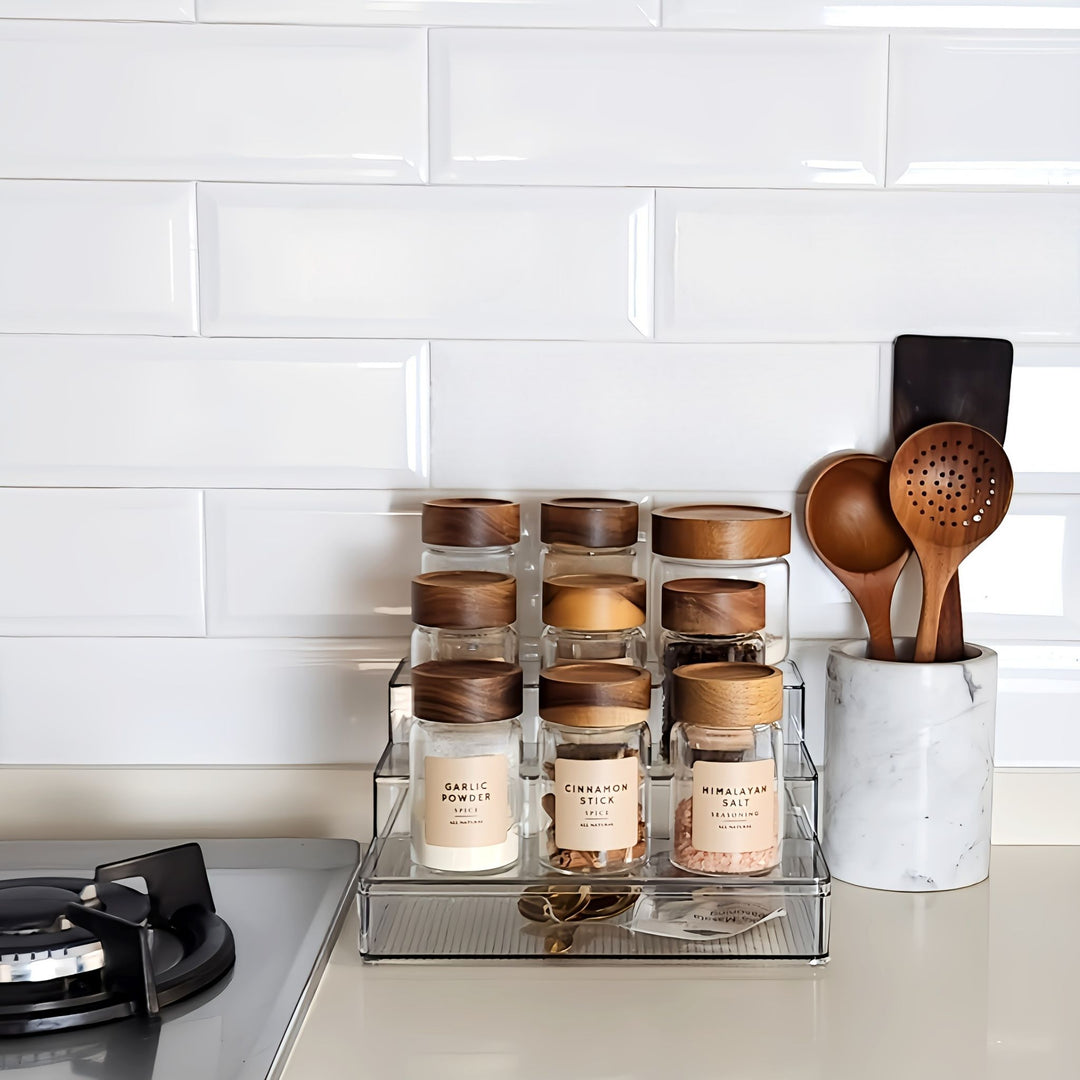 Kitchen counter with spice jars and wooden utensils against a white tiled wall.