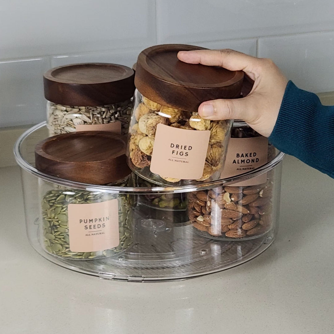 Hand holding a jar labeled 'Baked Almond' among other labeled jars on a clear rotating tray.